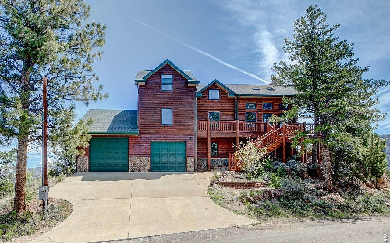 Exterior of the log lodge vacation rental in Estes Park with green garage doors and towering pines